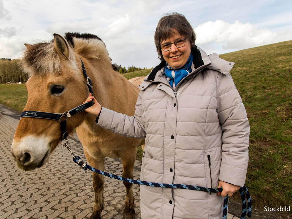 Eine Frau steht neben einem Pferd und lächelt.